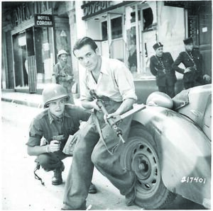 American_officer_and_French_partisan_crouch_behind_an_auto_during_a_street_fight_in_a_French_city